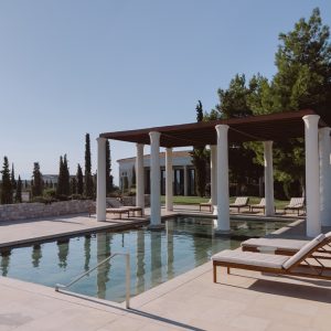 Pergola with columns near the pool with sun loungers surrounded by trees. Hotel Amanzoe, Greece